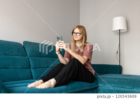 Beautiful blonde woman having fun online on her smartphone at home or hotel. Phone Communication and comfort concept. Smiling 30s woman daydreaming and holding mobile phone with copy space. Full body Beautiful blonde woman having fun online on her smartphone at home or hotel. Phone Communication and comfort concept. Smiling 30s woman daydreaming and holding mobile phone with copy space. Full body 120543609