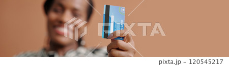 Smiling Woman Holding Credit Card Up Against Brown Background Smiling Woman Holding Credit Card Up Against Brown Background 120545217