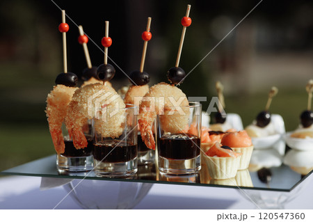 A table with a variety of appetizers and drinks, including shrimp, olives 120547360