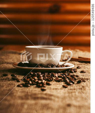 Cup of coffee with smoke and coffee beans on burlap on old wooden background Cup of coffee with smoke and coffee beans on burlap on old wooden background 120549486
