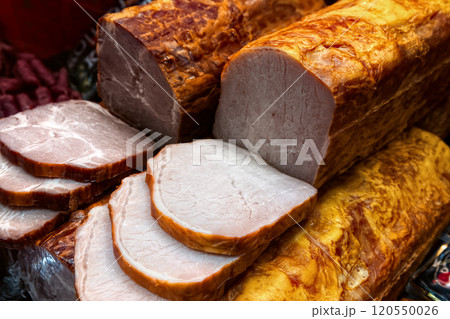 Various smoked pork hams in glass display case of butcher shop, top view. 120550026