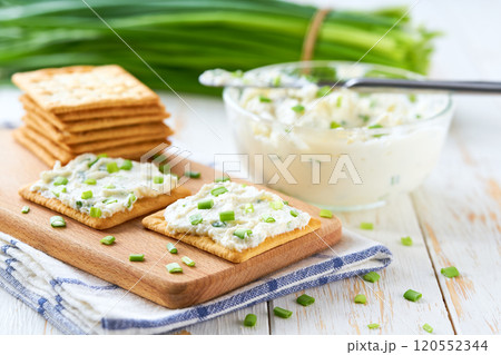 Glass bowl of cream cheese with spring onions and crackers, on a wooden table, selective focus. Glass bowl of cream cheese with spring onions and crackers, on a wooden table, selective focus. 120552344