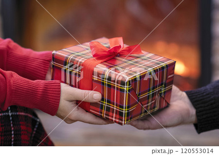 Man giving Christmas and New Year Gift box to woman in front of the fireplace with flame. 120553014