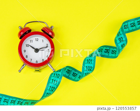 Red alarm clock and bright tape measure on yellow background with copy space Red alarm clock and bright tape measure on yellow background with copy space 120553857