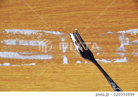 ショートケーキから剥がして木目調の机に置いたフィルムに付着しているクリームをフォークで掬っている光景 120553899