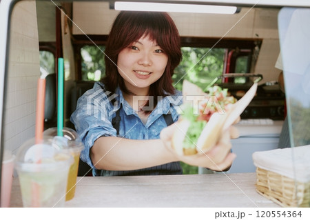 Medium close up portrait of smiling Asian cook demonstrating hot dog, focus on her face Medium close up portrait of smiling Asian cook demonstrating hot dog, focus on her face 120554364