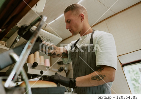 Low angle shot of focused Caucasian chef frying hot dog buns on grill in food truck 120554385