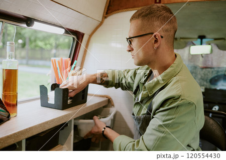 Side view of Caucasian young adult filling box with paper tissue while preparing for workday at food truck Side view of Caucasian young adult filling box with paper tissue while preparing for workday at food truck 120554430