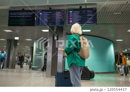 Caucasian senior woman passengers with suitcase using mobile phone booking hotel during waiting flight at boarding gate in airport terminal. Attractive female tourist travel by airplane on holiday Caucasian senior woman passengers with suitcase using mobile phone booking hotel during waiting flight at boarding gate in airport terminal. Attractive female tourist travel by airplane on holiday 120554437