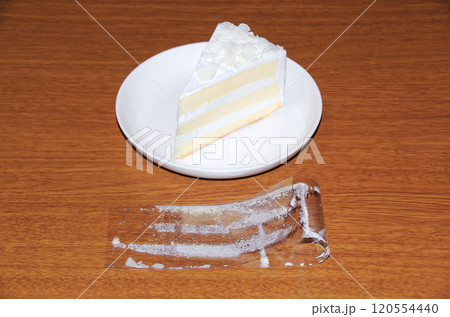 ショートケーキから剥がして折り曲げて木目調の机に置いたフィルムの内側に白いクリームが付着している状態 120554440