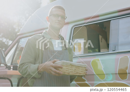 Portrait of young Caucasian food truck worker standing still with wicker box in hands illumined with warm sunrays Portrait of young Caucasian food truck worker standing still with wicker box in hands illumined with warm sunrays 120554465