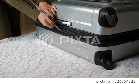 Close-up of woman zipping up suitcase filled with neatly packed clothes, excited for her upcoming adventure Close-up of woman zipping up suitcase filled with neatly packed clothes, excited for her upcoming adventure 120554523