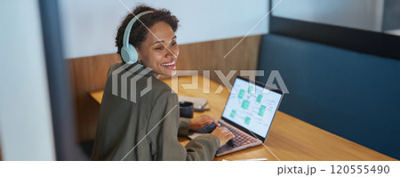 A woman wearing headphones is using a laptop computer at a table A woman wearing headphones is using a laptop computer at a table 120555490