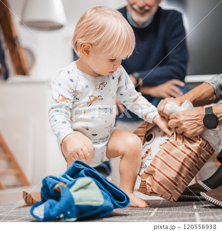 Cute little blond Caucasian toddler unpacking Christmas or Birthday present. Adorable small infant baby boy opening gift. 120556938
