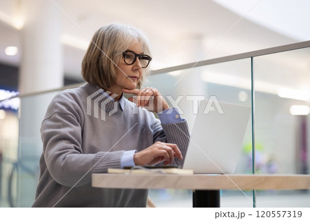 Senior woman working on laptop at a cafe in a modern shopping mall during the daytime, focused on Senior woman working on laptop at a cafe in a modern shopping mall during the daytime, focused on 120557319
