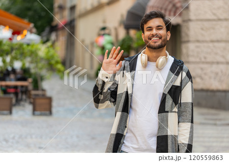 Indian young man smiling friendly at camera, hello waving hands gesturing hi, greeting on street 120559863