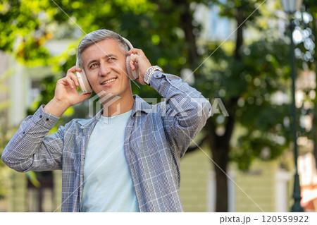 Young gray-haired man listening to music using wireless headphones and smartphone on city street Young gray-haired man listening to music using wireless headphones and smartphone on city street 120559922
