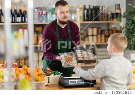 Friendly seller offers cookies to little customer in grocery store Friendly seller offers cookies to little customer in grocery store 120561619