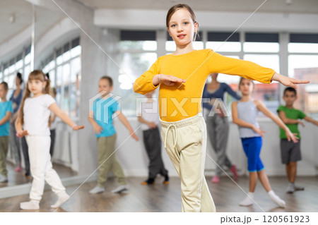 Positive juvenile girl engaged in hip-hop dance in training room with children's group 120561923