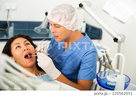 Focused man dentist examines a female patient with the help of working tools 120562051