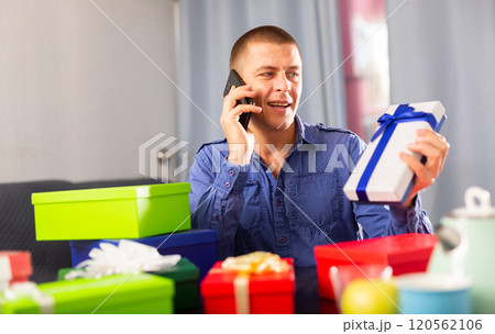 Man with boxes of gifts sits at table and talks on mobile phone Man with boxes of gifts sits at table and talks on mobile phone 120562106