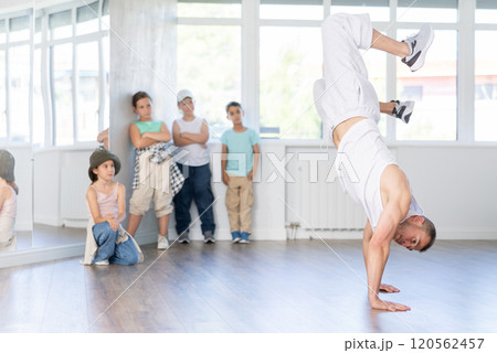 Experienced male trainer demonstrating to group of children dancers correct movements in hip-hop dance in choreography studio 120562457