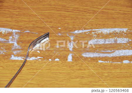 ショートケーキから剥がして木目調の机に置いたフィルムに付着しているクリームをフォークで掬っている光景 ショートケーキから剥がして木目調の机に置いたフィルムに付着しているクリームをフォークで掬っている光景 120563408