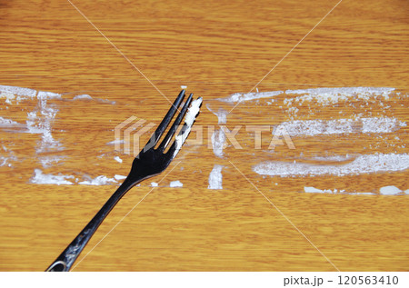 ショートケーキから剥がして木目調の机に置いたフィルムに付着しているクリームをフォークで掬っている光景 120563410