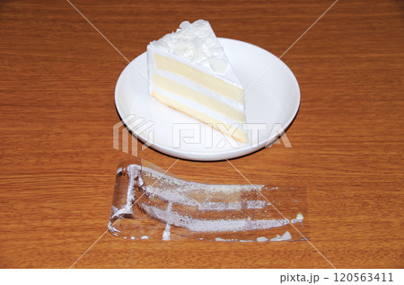 ショートケーキから剥がして折り曲げて木目調の机に置いたフィルムの内側に白いクリームが付着している状態 120563411