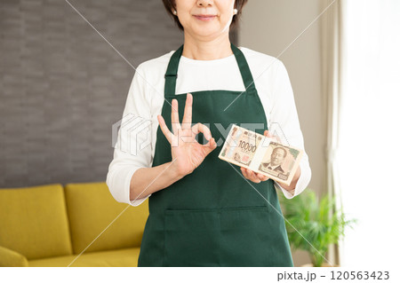 100万円の札束を持って丸サインをする緑のエプロンをしたミドル〜シニア女性の主婦 100万円の札束を持って丸サインをする緑のエプロンをしたミドル〜シニア女性の主婦 120563423