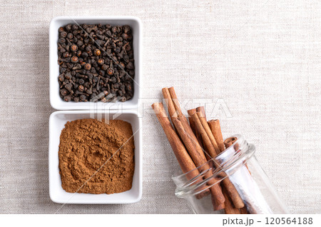 Cassia cinnamon powder and buds in white bowls, sticks in a glass jar, on linen fabric, with empty space for text. Whole and grated dried bark of Chinese cinnamon, Cinnamomum cassia, used as a spice. 120564188