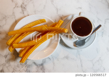 Traditional spanish dessert churros - fried choux pastry and hot chocolate mug on a table Traditional spanish dessert churros - fried choux pastry and hot chocolate mug on a table 120566517
