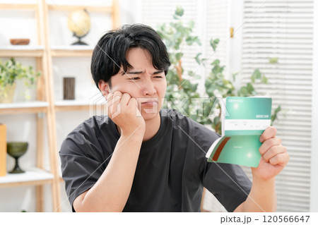 通帳を持って悩む男性 120566647