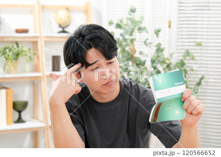 通帳を持って悩む男性 120566652