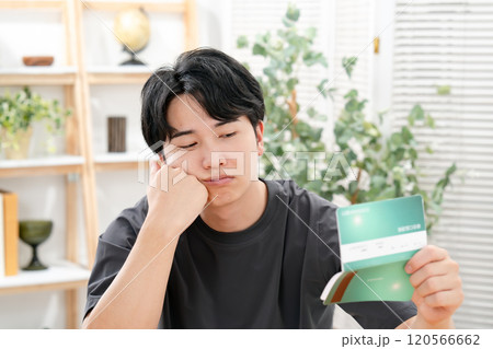 通帳を持って悩む男性 120566662
