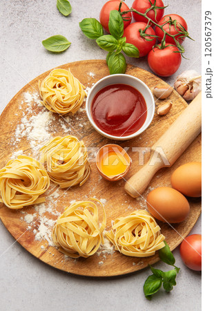 Fresh tagliatelle pasta nests with tomatoes, basil, eggs, flour and tomato sauce on wooden board 120567379