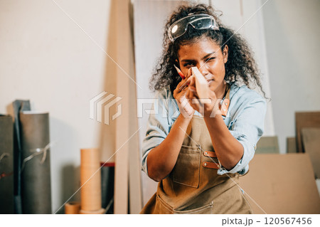 Carpenter woman holding and inspecting a piece of wood in a workshop, surrounded by tools and materials. Focused on woodworking and craftsmanship. National Carpenters Day celebration 120567456