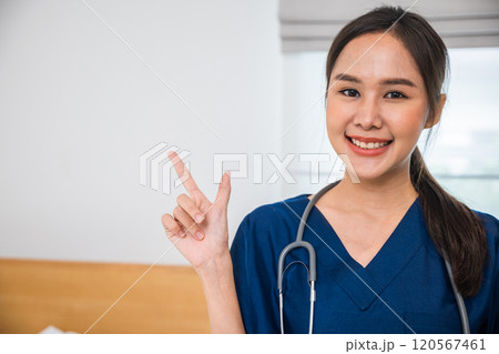 Portrait of happy woman nurse employee healthcare worker pointing finger on side away gesture, Asian female healthcare professional in scrubs standing in a hospital room, Health care and medical 120567461