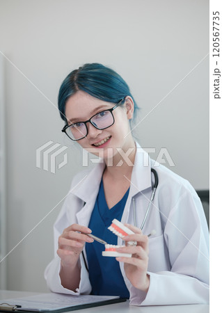 A woman in a white lab coat holding a pair of teeth 120567735