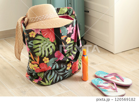 Summer hat with bow on beach bag near flip flops at home. Summer and vacation. Traveling and packing for vacation. Summer hat with bow on beach bag near flip flops at home. Summer and vacation. Traveling and packing for vacation. 120569182