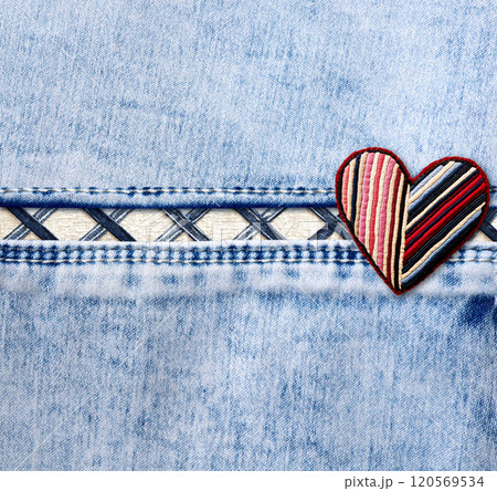 Light blue denim background with a seam and felt heart in patchwork style. Square denim jeans fabric texture with heart-shaped textile patch. Valentine's day denim backdrop. Copy space for text 120569534