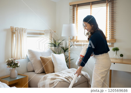 Cheerful young woman using a cordless vacuuming floor in living room Cheerful young woman using a cordless vacuuming floor in living room 120569686