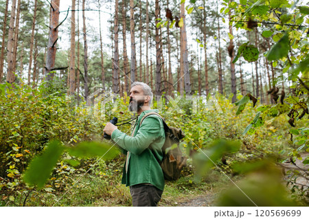 Tourist standing in the middle of nature, using binoculars to observe nature and wildlife in the forest. Tourist standing in the middle of nature, using binoculars to observe nature and wildlife in the forest. 120569699
