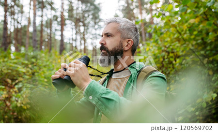 Tourist standing in the middle of nature, using binoculars to observe nature and wildlife in the forest. Tourist standing in the middle of nature, using binoculars to observe nature and wildlife in the forest. 120569702