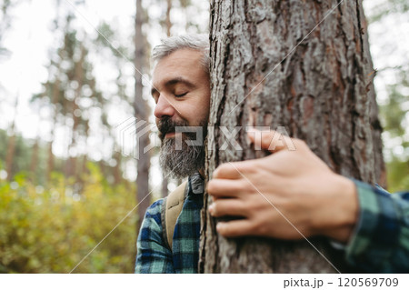 Handsome man standing in forest with closed eyes, hugging tree. Peaceful atmosphere of the nature, forestbathing. Handsome man standing in forest with closed eyes, hugging tree. Peaceful atmosphere of the nature, forestbathing. 120569709