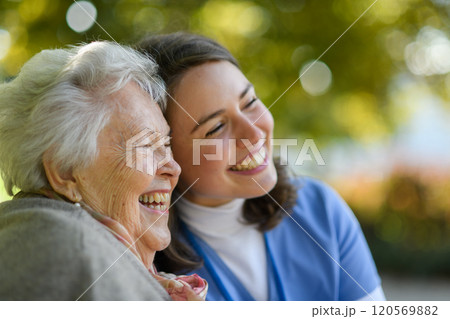 Portrait of nurse and elderly woman in autmn park. Young caregiver spending time with senior patient. 120569882