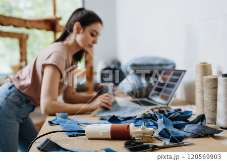 Young businesswoman working on laptop on workbench, standing by wooden loom. Upcycled textile, small weaving business and circular economy. Young businesswoman working on laptop on workbench, standing by wooden loom. Upcycled textile, small weaving business and circular economy. 120569903