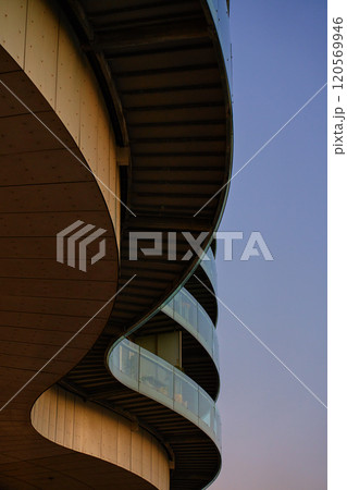 Modern round residential building with balconies at sunset. Contemporary architecture with curved design. Minimalistic style of apartment building with glass facade 120569946