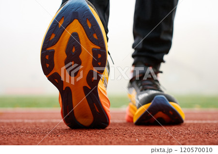 Close-up of running shoes sole with athlete training at stadium. Sportsman legs in sport sneakers on track surface 120570010