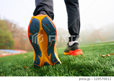 Close-up of running shoes sole with athlete walking on artificial grass. Sportsman legs in sport sneakers on green grass 120570011